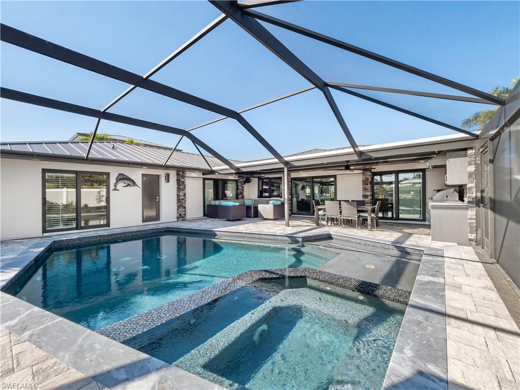 Combined pool / hot tub featuring a sunroom, a lanai, a patio, and an outdoor kitchen / dining area