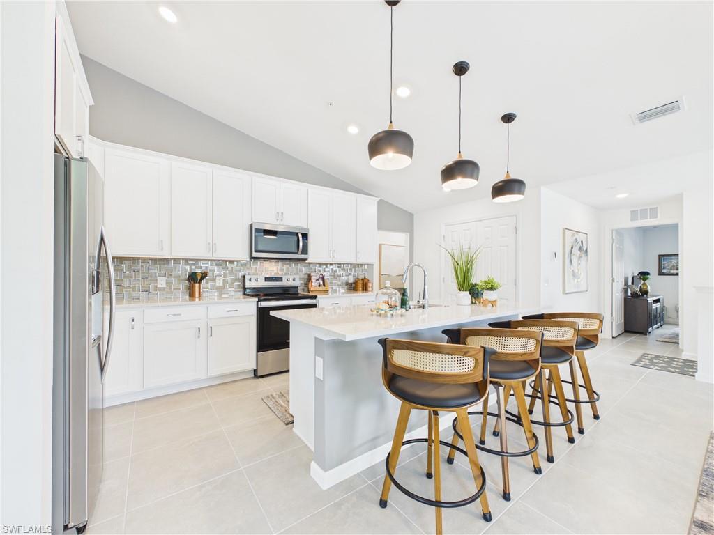 Kitchen with stainless steel appliances, a kitchen breakfast bar, vaulted ceiling, an island with sink, and white cabinetry