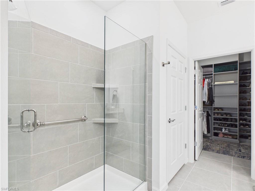 Full bathroom featuring a shower stall, a spacious closet, and light tile patterned floors