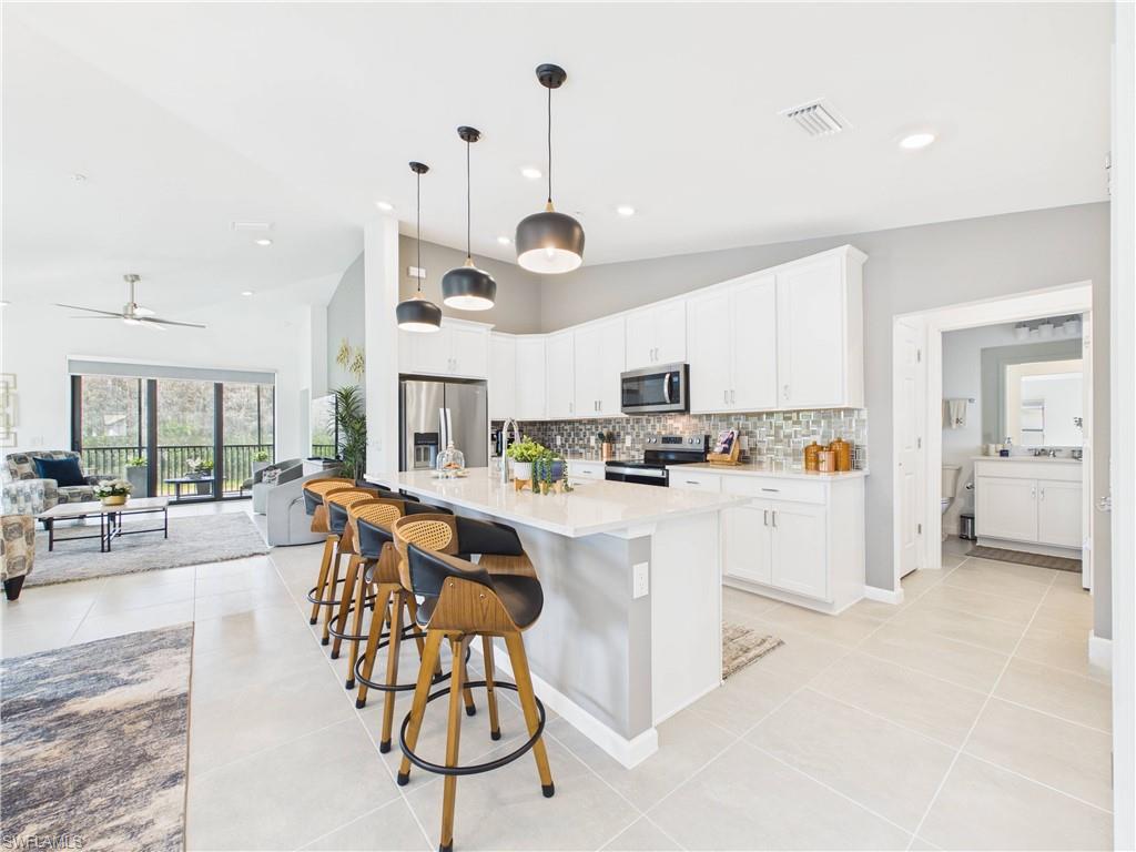 Kitchen with stainless steel appliances, a center island with sink, a breakfast bar, white cabinets, and vaulted ceiling