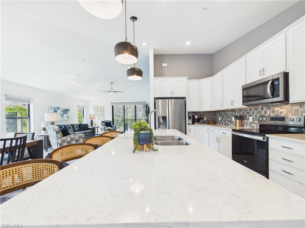 Kitchen with stainless steel appliances, decorative light fixtures, white cabinetry, tasteful backsplash, and light stone countertops