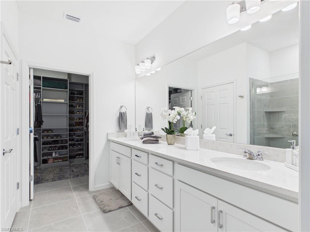 Bathroom featuring double vanity, a stall shower, light tile patterned floors, and a spacious closet