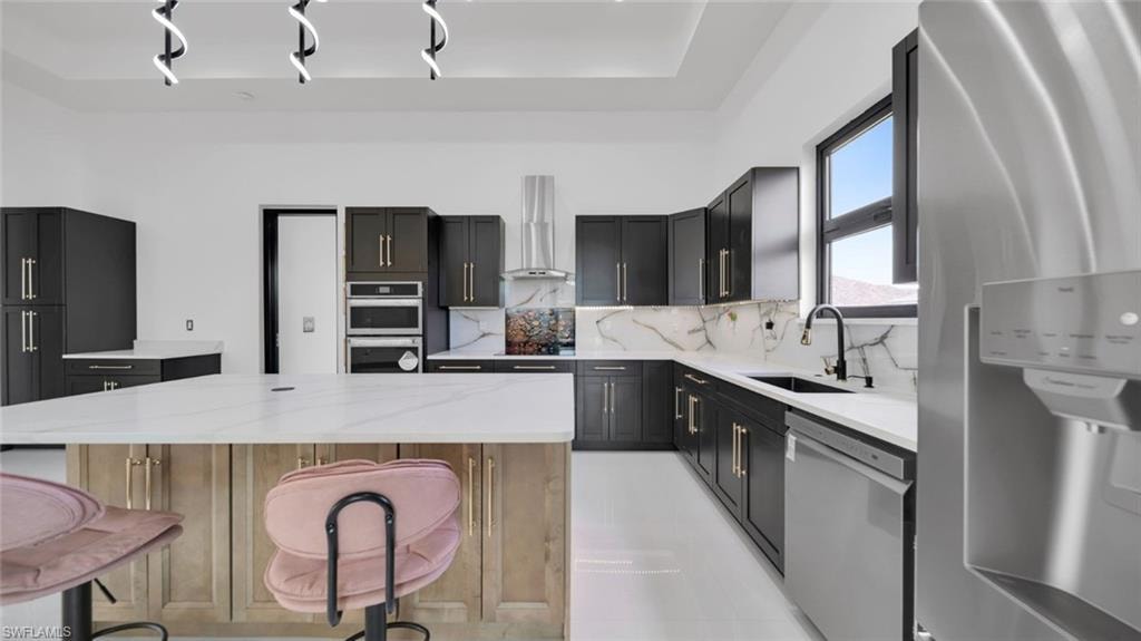 Kitchen featuring stainless steel appliances, light stone countertops, a center island, decorative backsplash, and a breakfast bar area