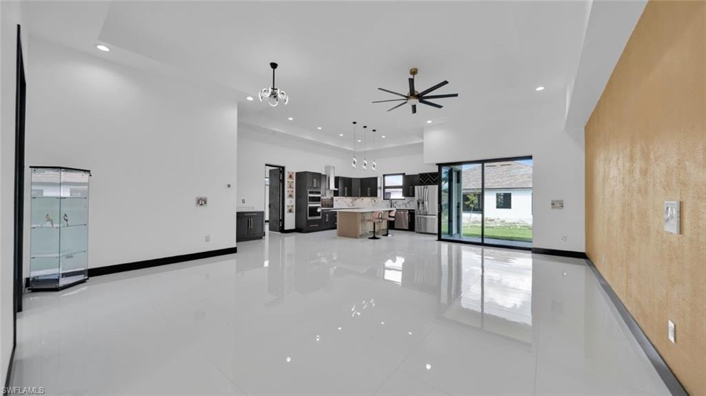 Unfurnished living room with a high ceiling, ceiling fan, and a chandelier