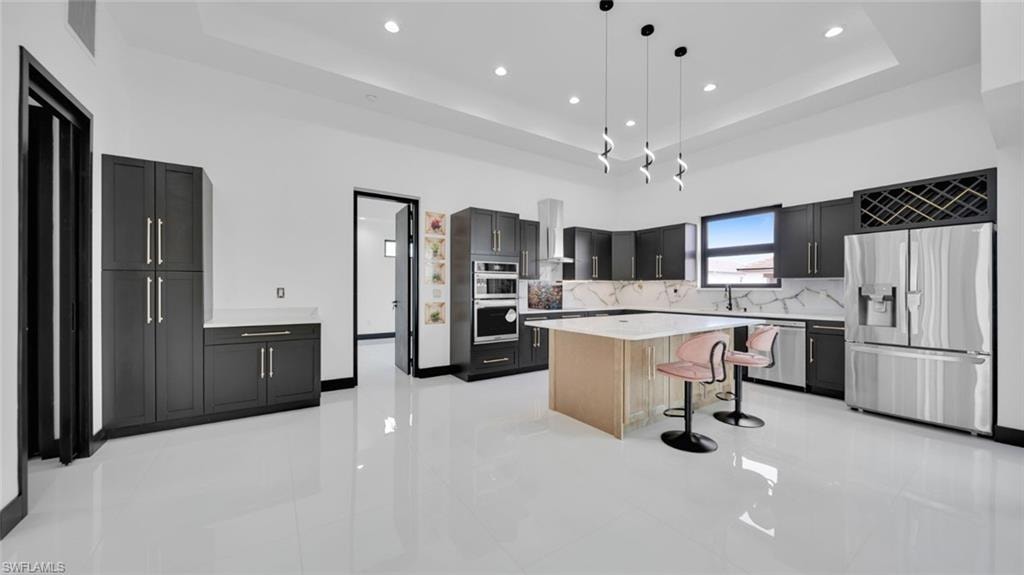 Kitchen with stainless steel appliances, pendant lighting, a breakfast bar area, light stone countertops, and a high tray ceiling