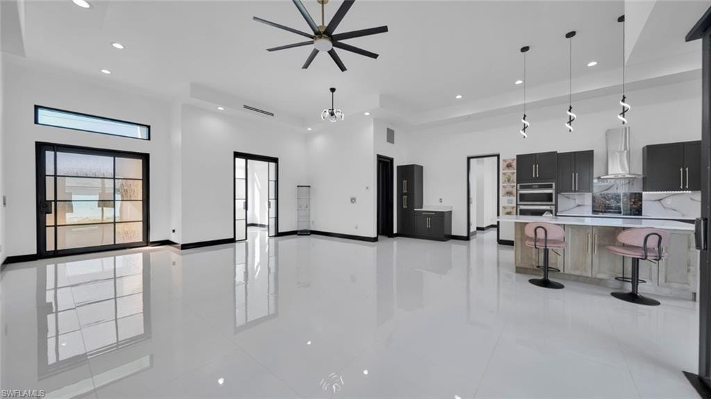 Kitchen featuring open floor plan, a kitchen bar, decorative light fixtures, a high ceiling, and dark cabinets