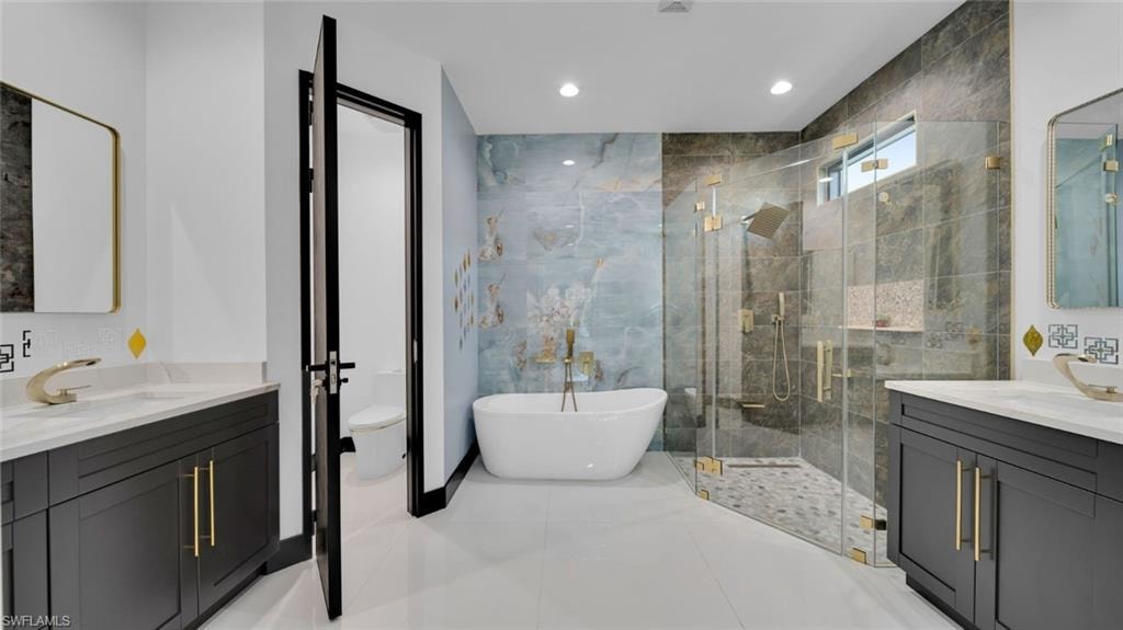 Full bathroom featuring two vanities, a freestanding bath, a marble finish shower, and recessed lighting
