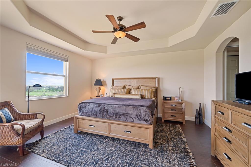 Bedroom featuring dark wood-style floors, a raised ceiling, arched walkways, and ceiling fan