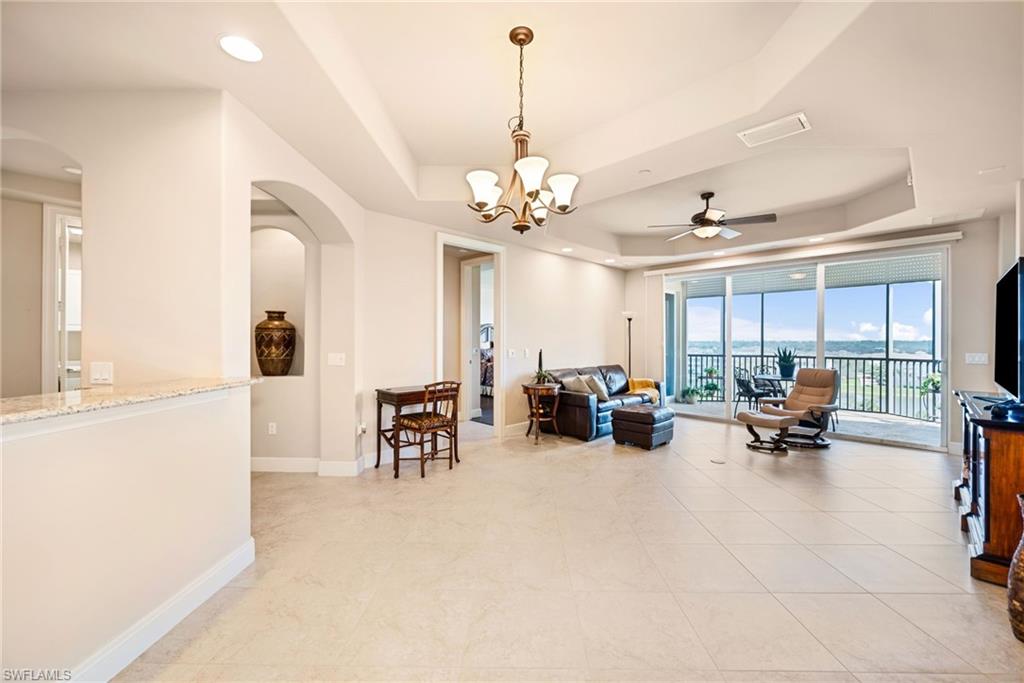 Living room with arched walkways, a ceiling fan, a tray ceiling, and hanging lights