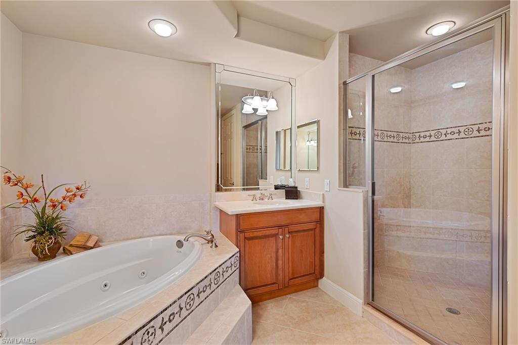 Full ensuite featuring vanity, a shower stall, light tile patterned floors, and a whirlpool tub