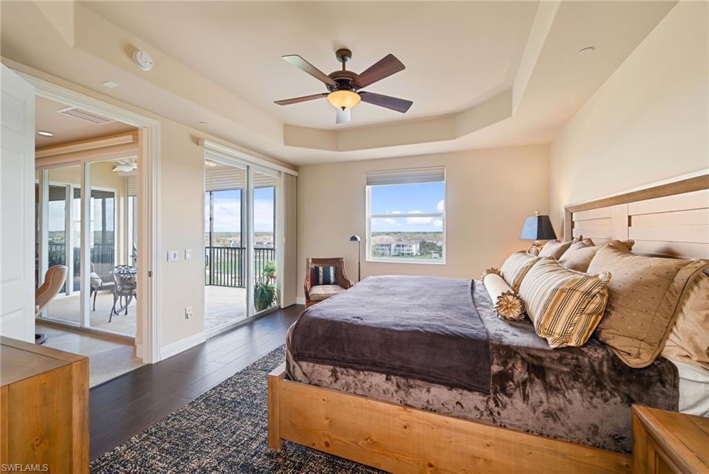Primary Bedroom featuring dark wood-style flooring, access to exterior, ceiling fan, and a tray ceiling