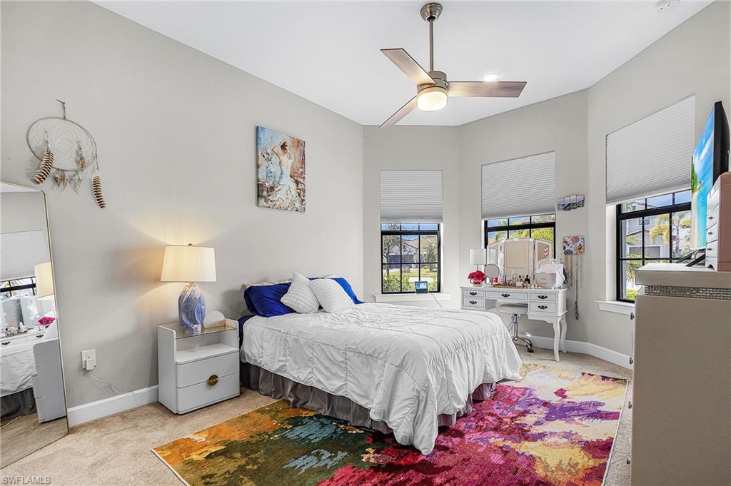 Bedroom featuring light colored carpet, multiple windows, and a ceiling fan