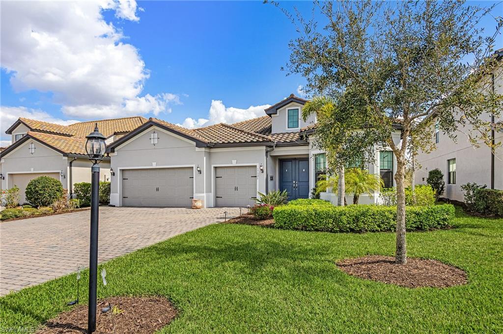 Mediterranean / spanish home with decorative driveway, stucco siding, a garage, a tiled roof, and a front lawn