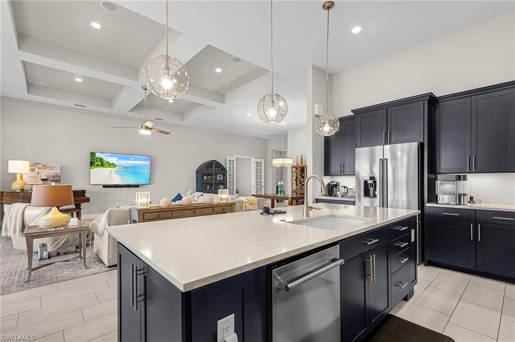 Kitchen featuring dark cabinetry, stainless steel appliances, open floor plan, pendant lighting, and light stone countertops