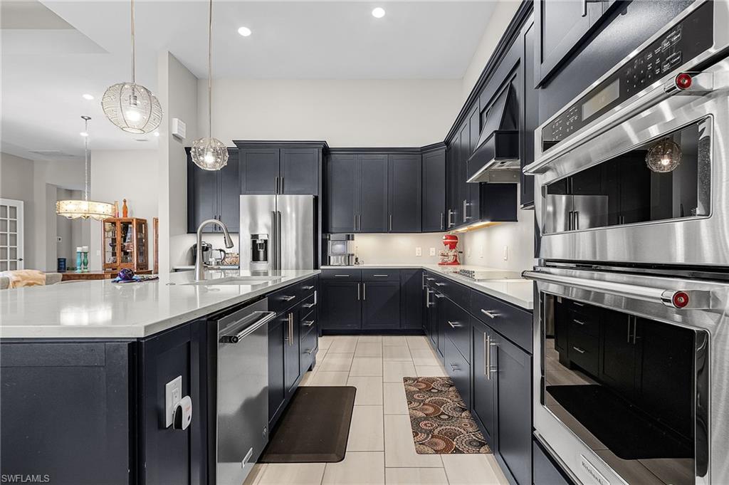 Kitchen with stainless steel appliances, dark cabinets, light stone countertops, and a spacious island