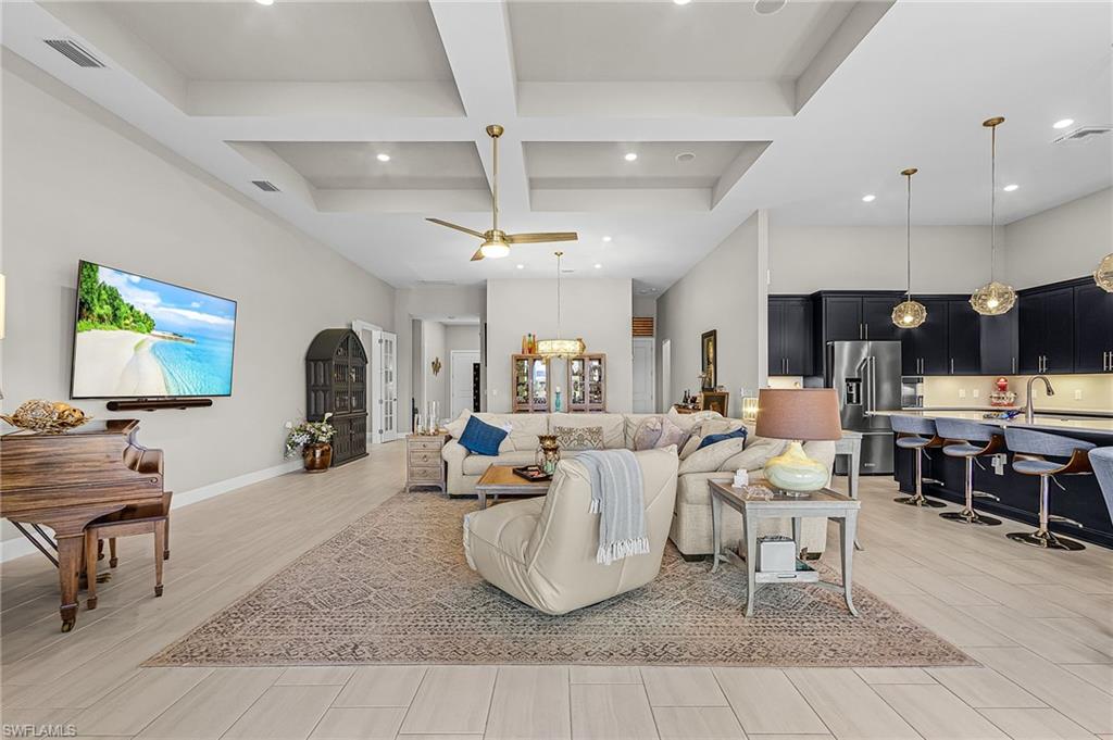Living area featuring coffered ceiling, light wood-style floors, ceiling fan, and hanging lights