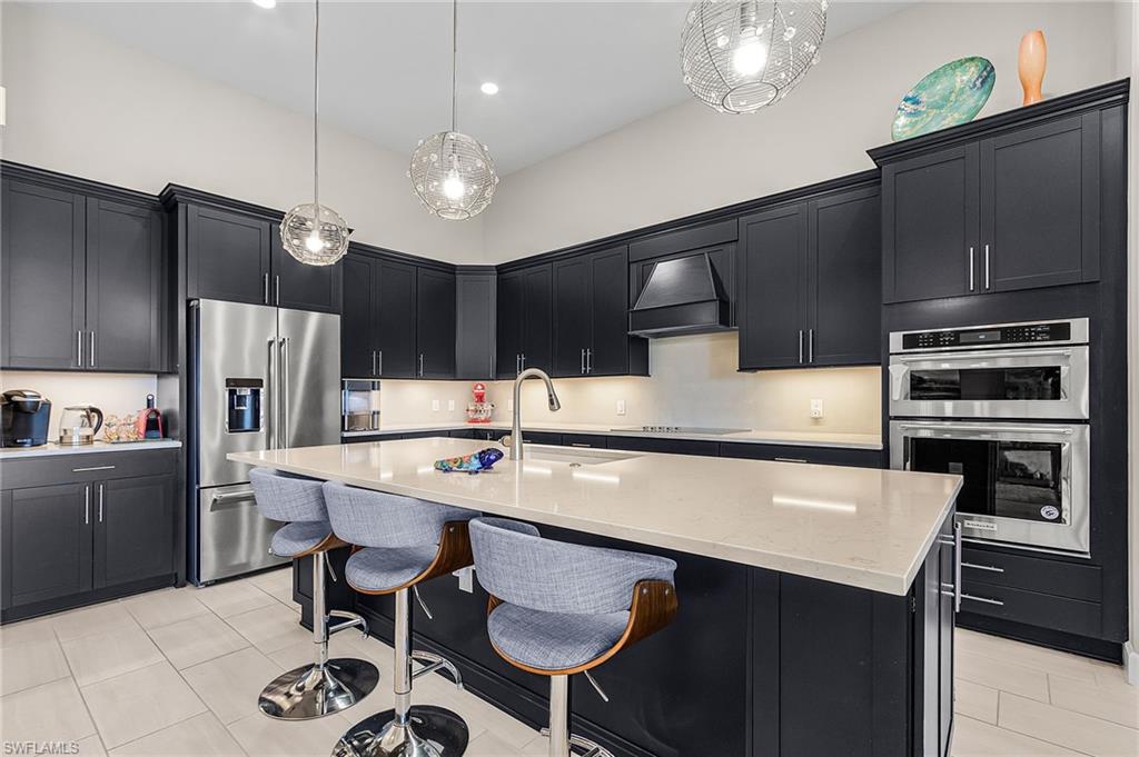 Kitchen featuring dark cabinetry, stainless steel appliances, a kitchen bar, light stone counters, and a high ceiling
