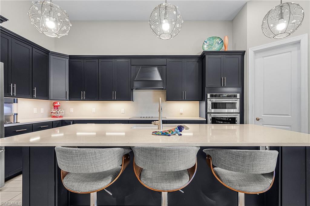 Kitchen featuring dark cabinets, a breakfast bar area, light stone counters, and a kitchen island with sink