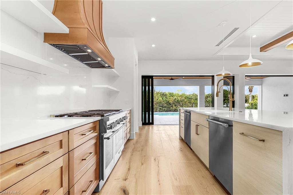 Kitchen featuring stainless steel appliances, light wood-style floors, light wood finish cabinets, pendant lighting, and light stone countertops