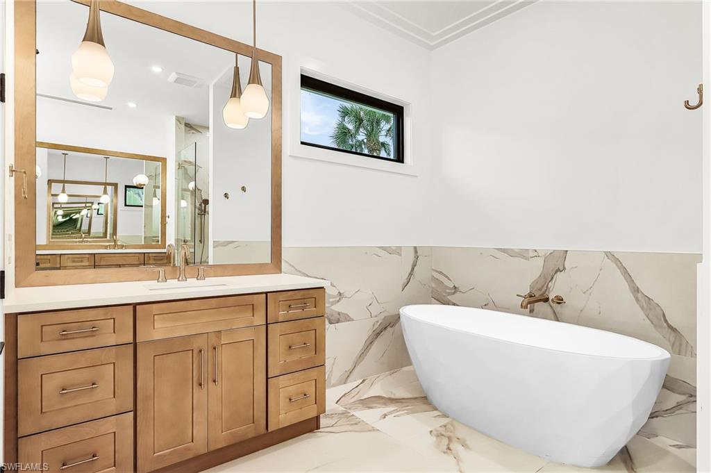 Full bath featuring vanity, light marble finish flooring, wainscoting, and a freestanding bath