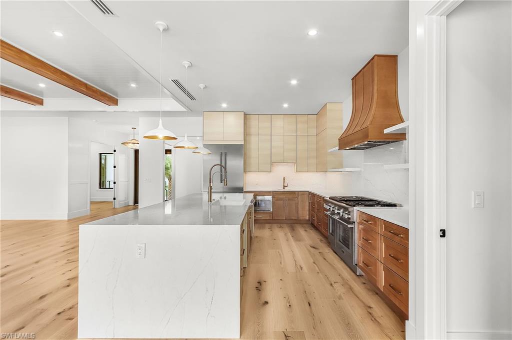 Kitchen featuring beamed ceiling, light stone counters, high end appliances, light wood-style flooring, and backsplash