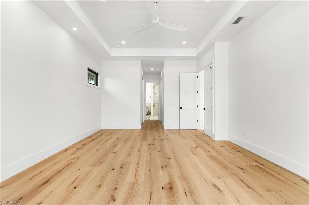 Unfurnished bedroom with recessed lighting, light wood-type flooring, a raised ceiling, ensuite bathroom, and a closet