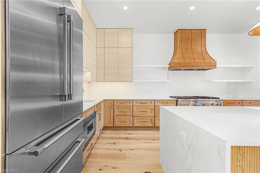 Kitchen featuring stainless steel appliances, open shelves, decorative backsplash, light wood finish cabinetry, and light wood-style floors