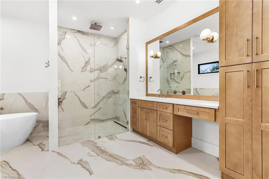 Full bathroom with vanity, a marble finish shower, a freestanding tub, light marble finish floors, and stone wall
