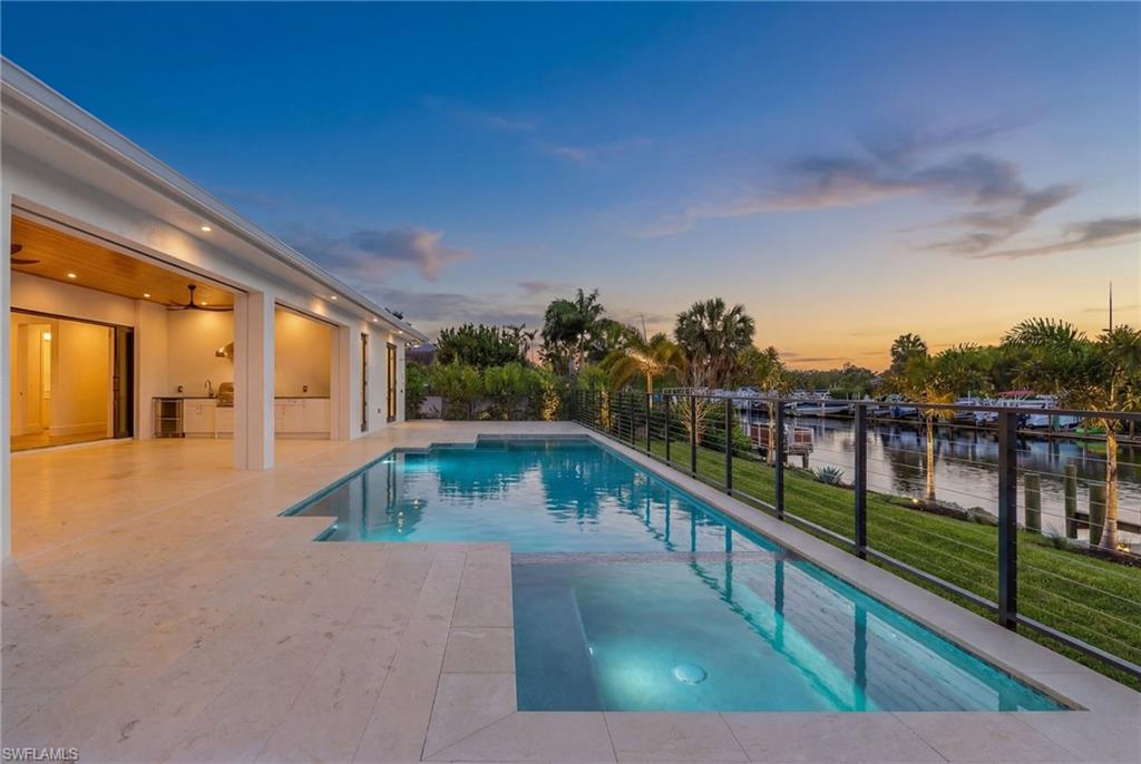Pool at dusk with a patio area, a pool with connected hot tub, a water view, and an outdoor kitchen