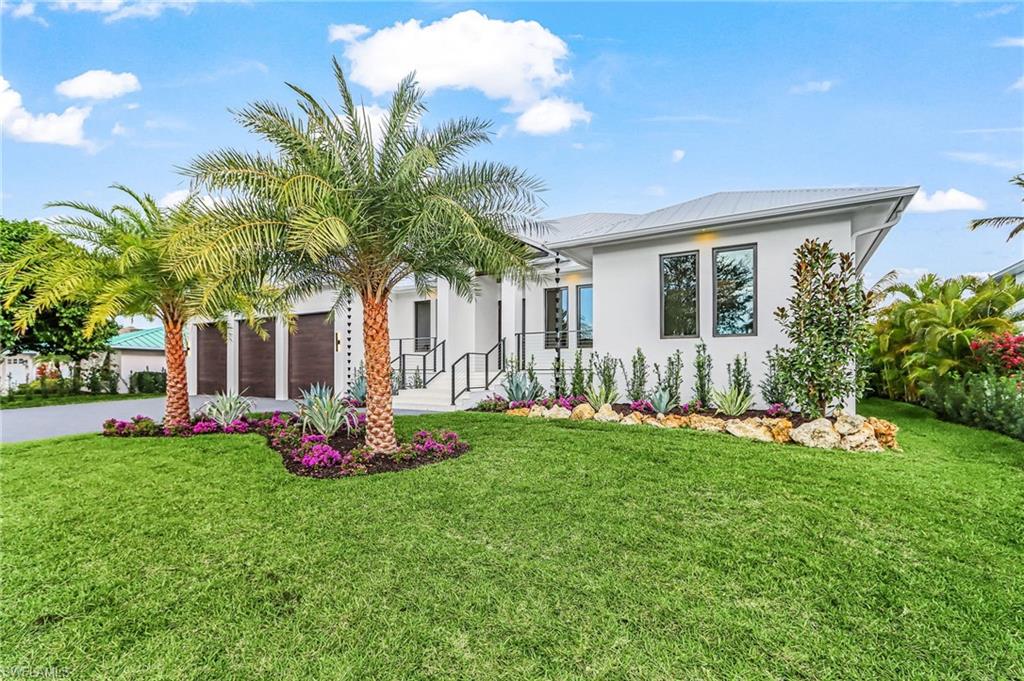 Back of house with stucco siding, driveway, a lawn, an attached garage, and a metal roof