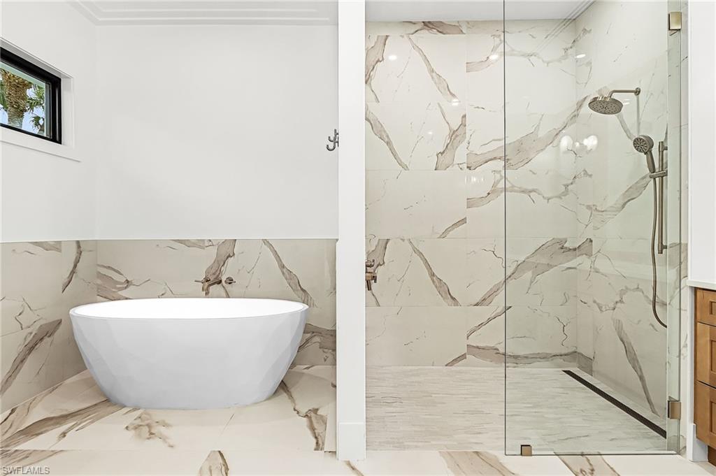 Full bath featuring a marble finish shower, a freestanding bath, and light marble finish floors