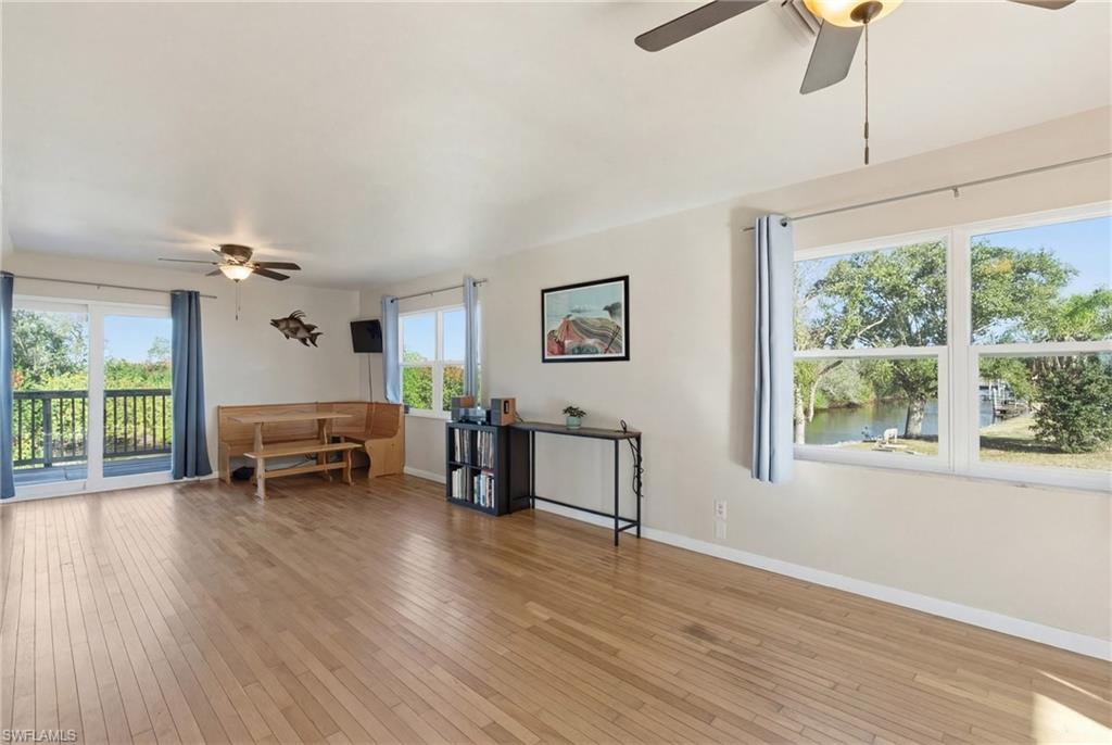 Living room featuring light wood-style floors, a ceiling fan, healthy amount of natural light, and a stone fireplace