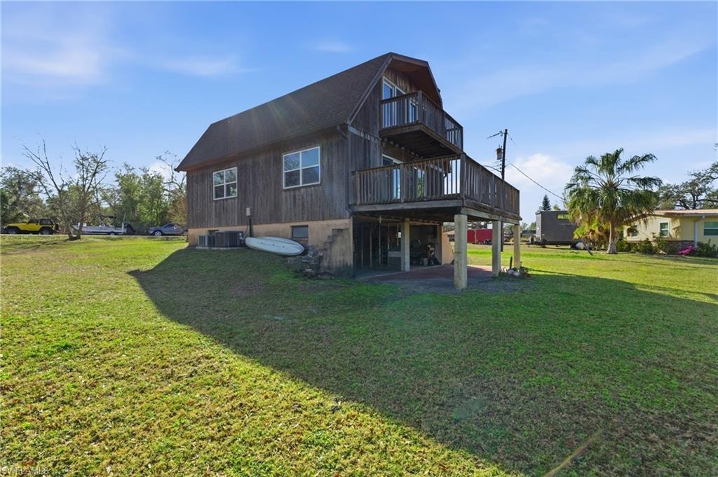 Back of property with a lawn, a patio, a wooden deck, and a balcony