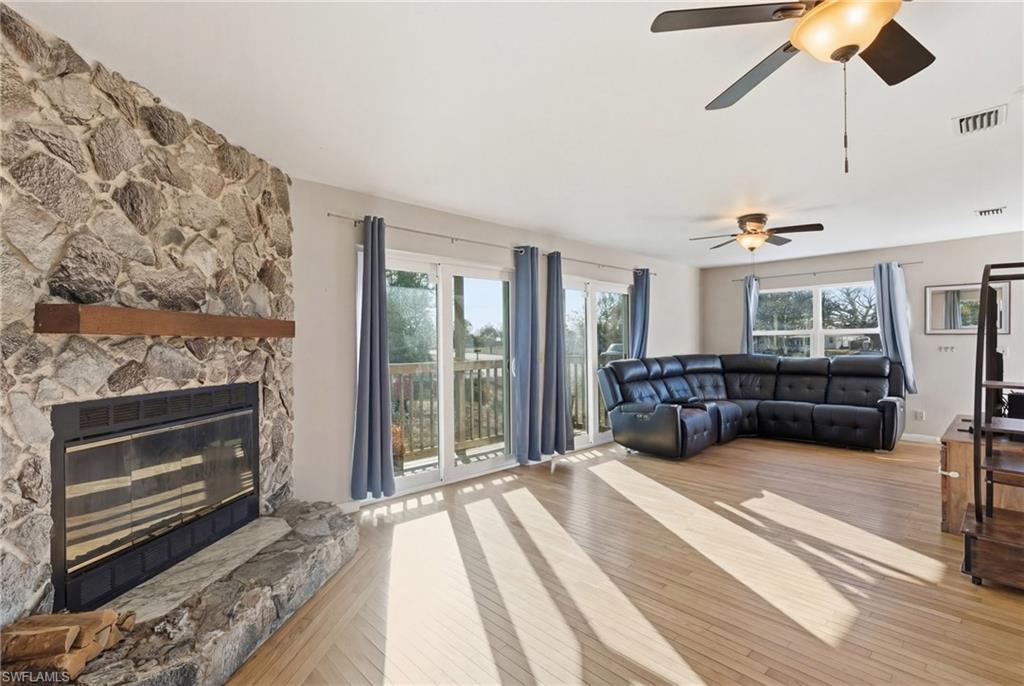 Living room with light wood finished floors, a stone fireplace, and a ceiling fan