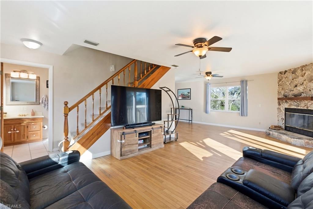 Unfurnished living room with light wood-style floors, a ceiling fan, a stone fireplace, and healthy amount of natural light