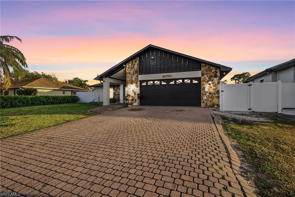 View of front of property featuring a gate, decorative driveway, a garage, and stone siding