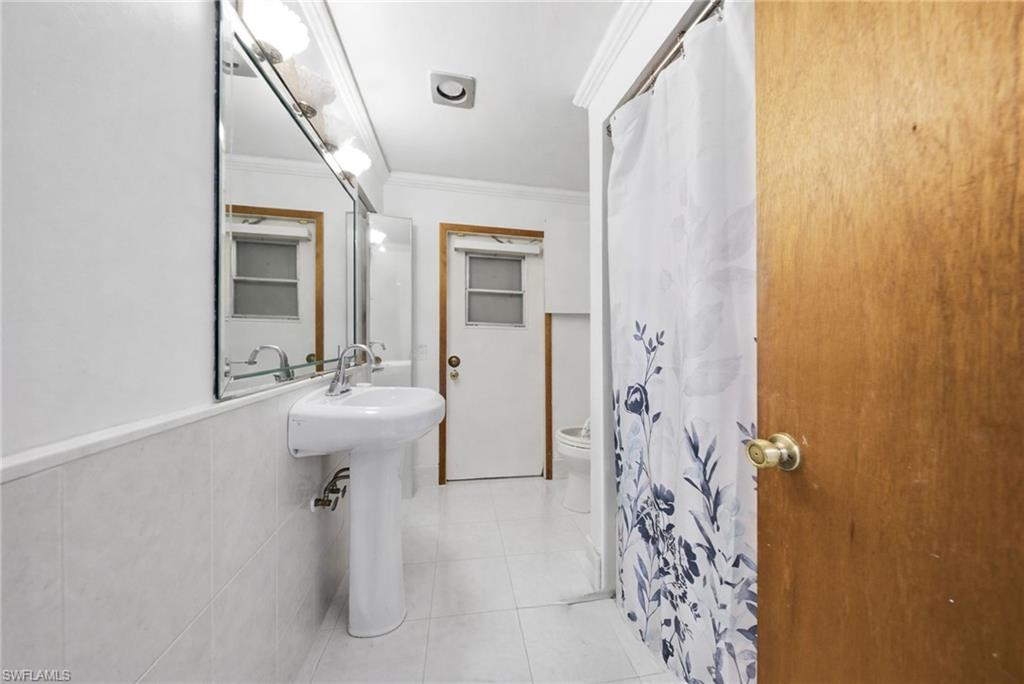 Full bath featuring ornamental molding, a shower with shower curtain, and light tile patterned floors
