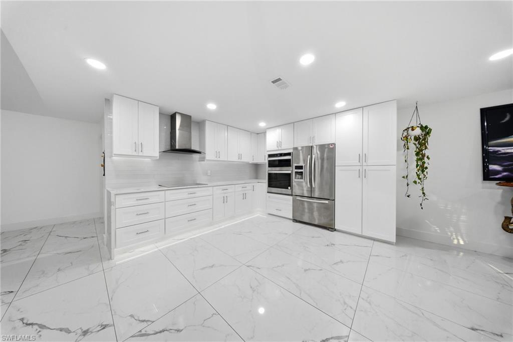 Kitchen with white cabinets, stainless steel appliances, decorative backsplash, light marble finish floors, and recessed lighting