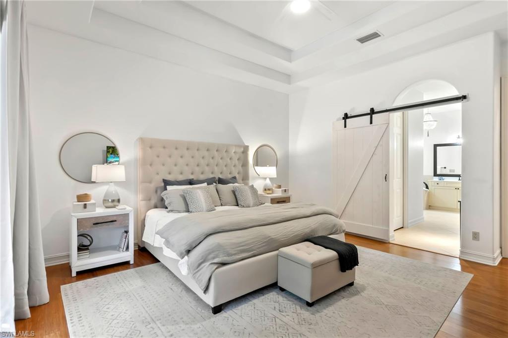Bedroom featuring a barn door, baseboards, visible vents, a raised ceiling, and wood finished floors