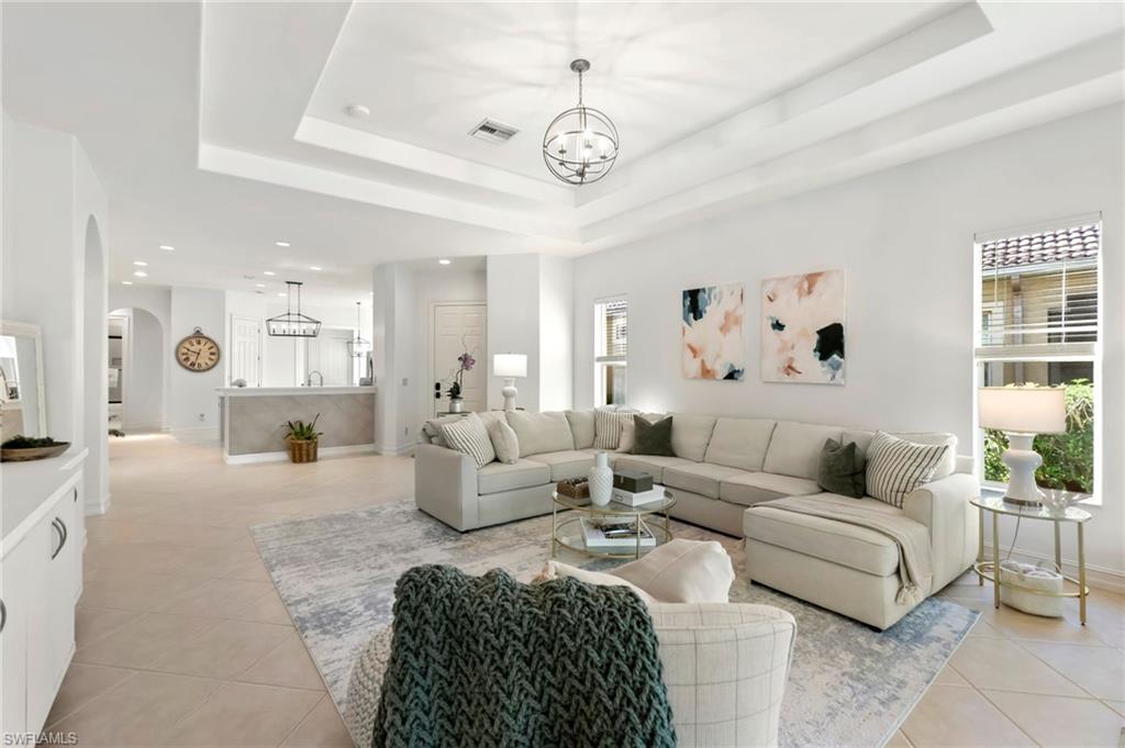 Living room featuring arched walkways, light tile patterned floors, a raised ceiling, visible vents, and a chandelier