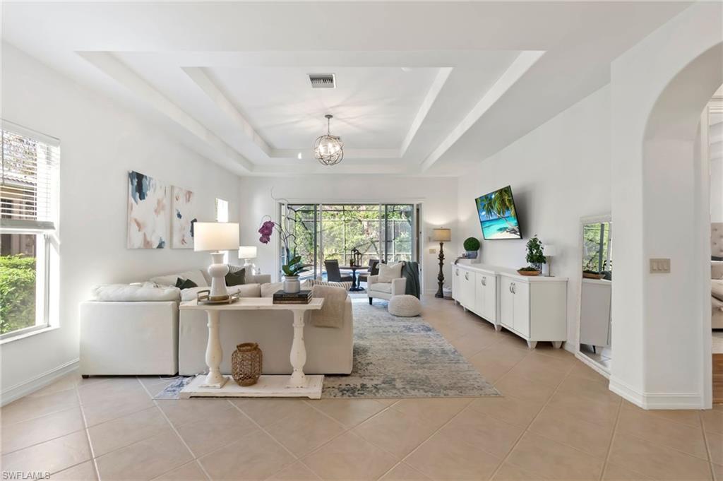 Living area with light tile patterned floors, visible vents, arched walkways, a tray ceiling, and a notable chandelier