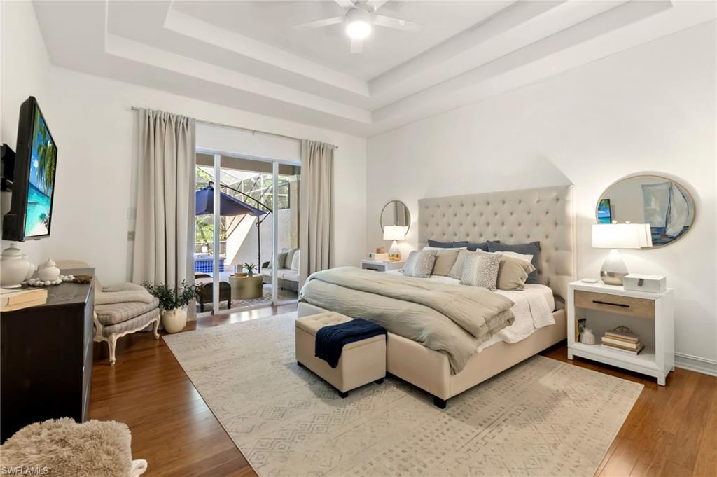 Bedroom with baseboards, a ceiling fan, wood finished floors, access to outside, and a tray ceiling