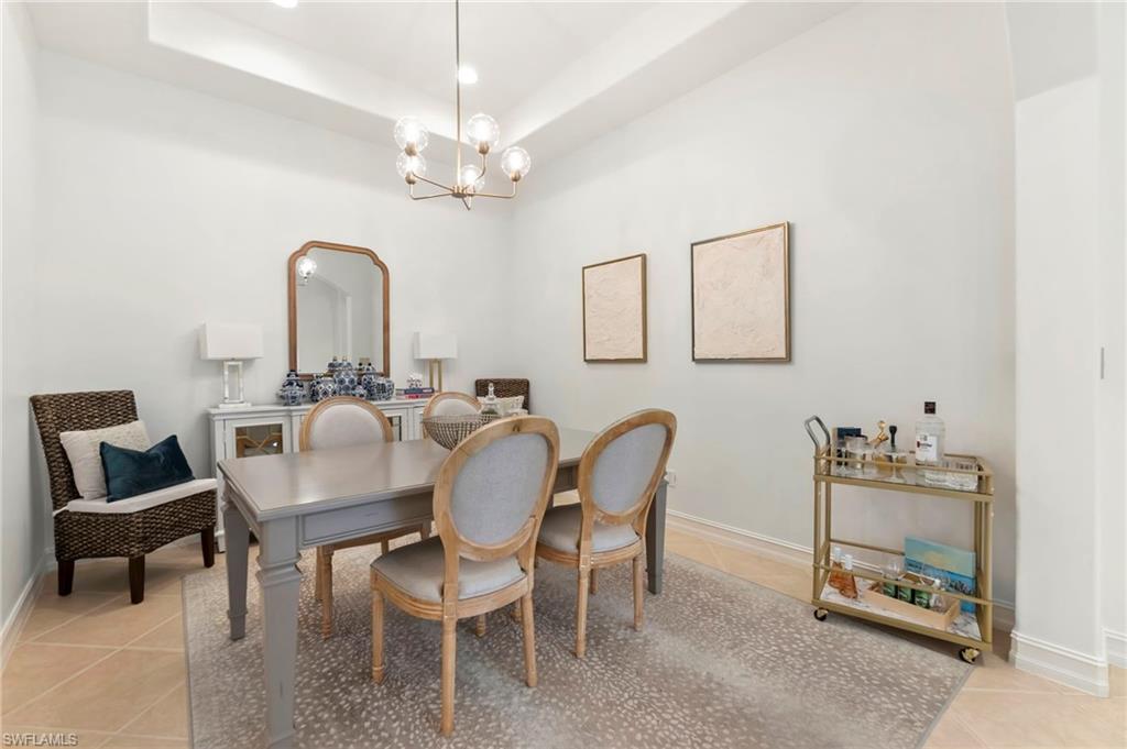 Dining room with light tile patterned floors, baseboards, a tray ceiling, and an inviting chandelier