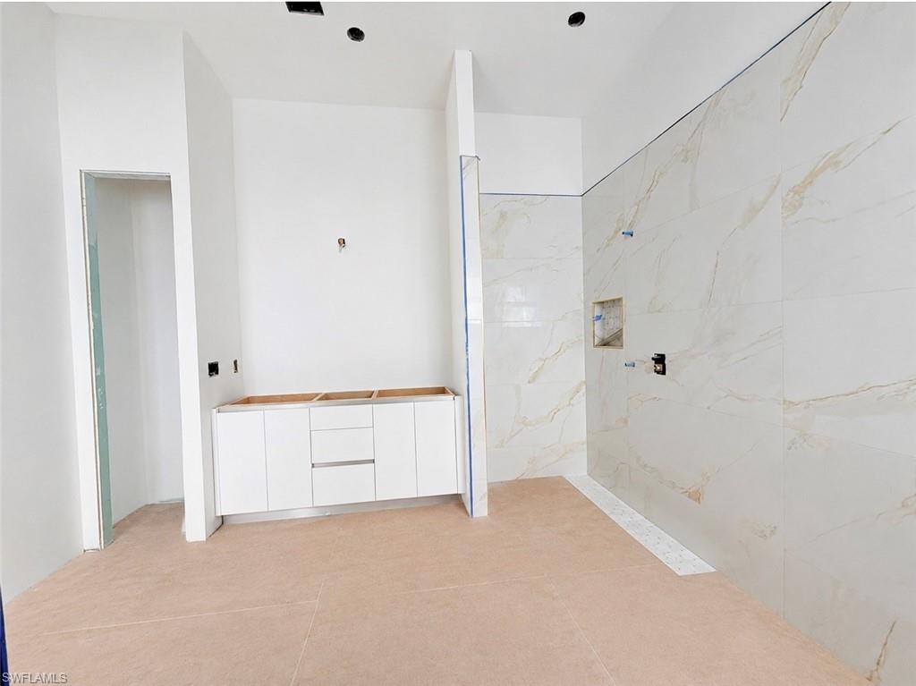Spacious bathroom featuring a white vanity cabinet, large format floor tile, and a walk-in shower with full-height tile surround and integrated niche