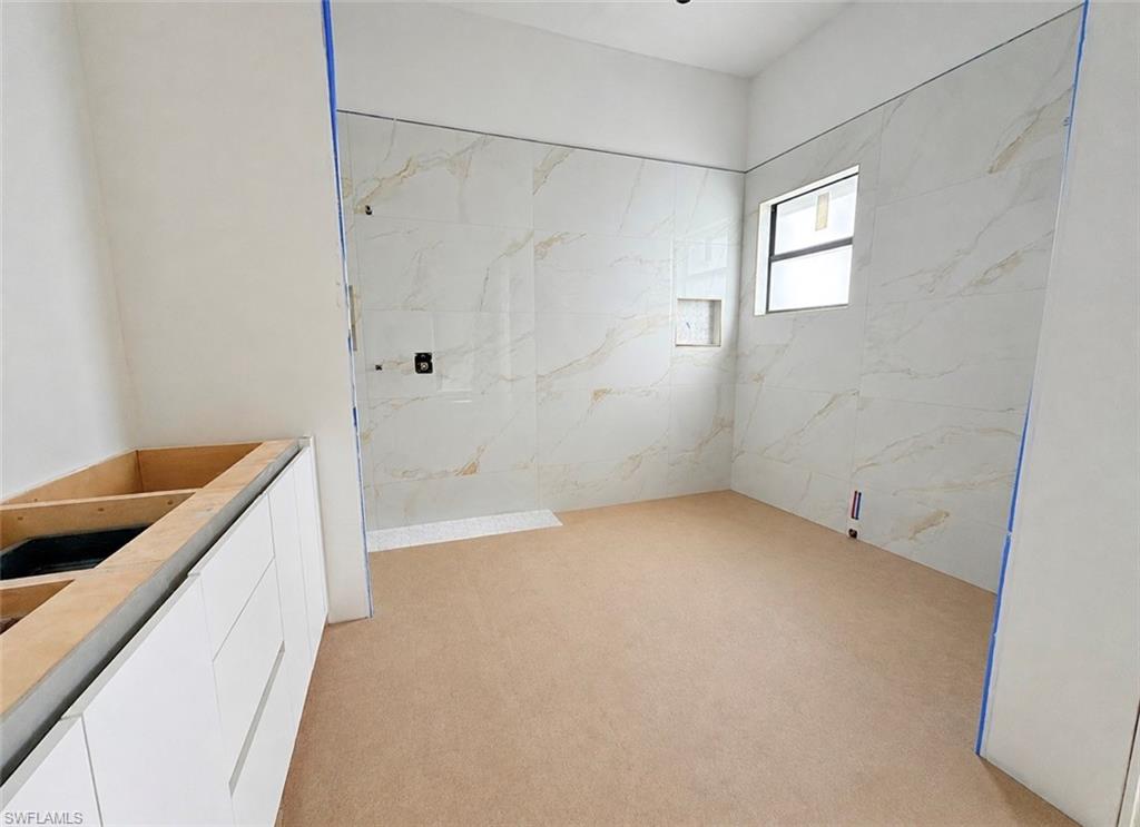 Spacious bathroom featuring large format wall tiles, a built-in shower niche, a window with an aluminum frame, and a vanity cabinet base
