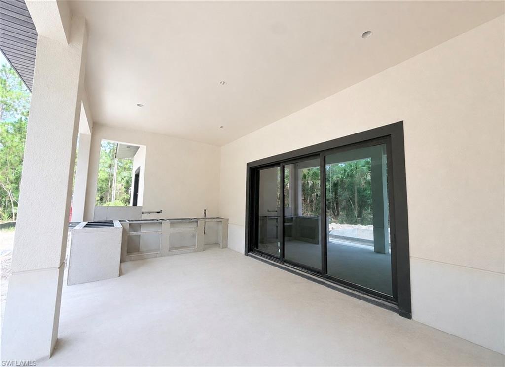 Covered patio with recessed lighting, built-in outdoor kitchen base, and large sliding glass doors