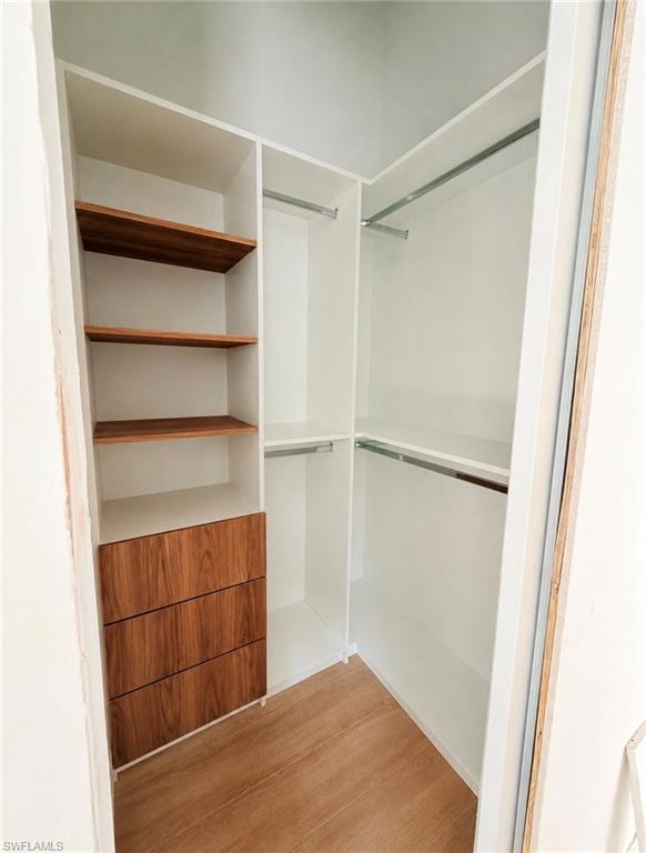 Custom closet system featuring white cabinetry, integrated wood-finish drawers, wood-finish shelving, and multiple hanging rods