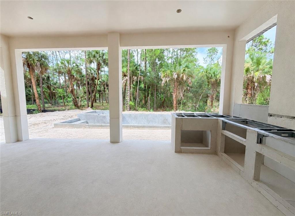 Spacious covered patio with outdoor kitchen framing, recessed lighting, and an adjacent concrete pool structure