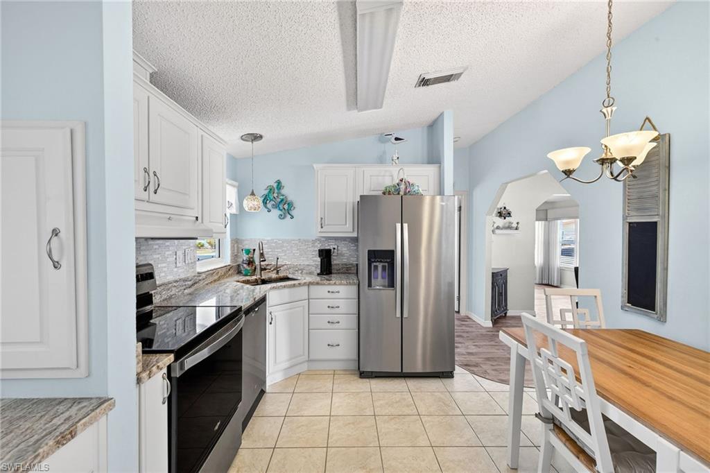 Kitchen with stainless steel appliances, white cabinets, light stone countertops, and arched walkways