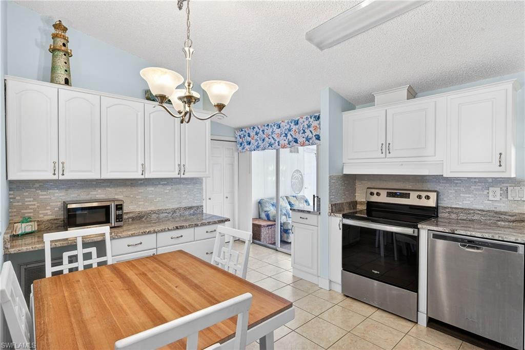 Kitchen with stainless steel appliances, white cabinetry, light stone counters, backsplash, and light tile patterned flooring